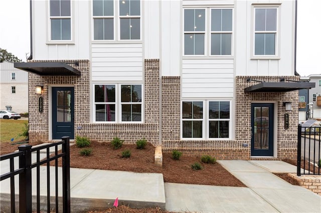 view of exterior entry featuring brick siding, board and batten siding, and fence