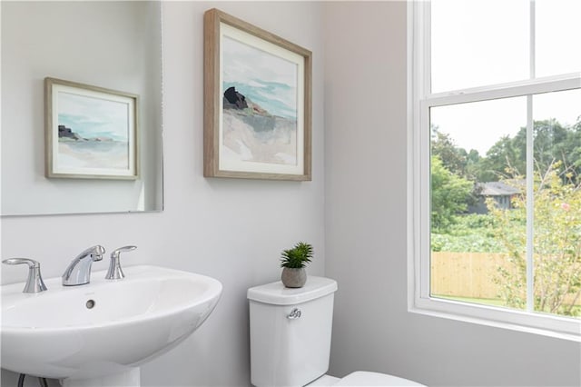 half bathroom featuring toilet, a healthy amount of sunlight, and a sink