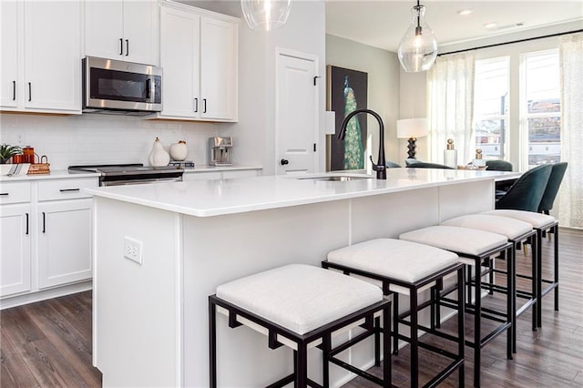 kitchen featuring a center island with sink, a sink, tasteful backsplash, dark wood finished floors, and appliances with stainless steel finishes