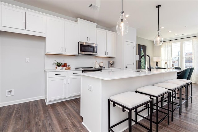 kitchen with a center island with sink, a sink, stainless steel microwave, tasteful backsplash, and white cabinetry