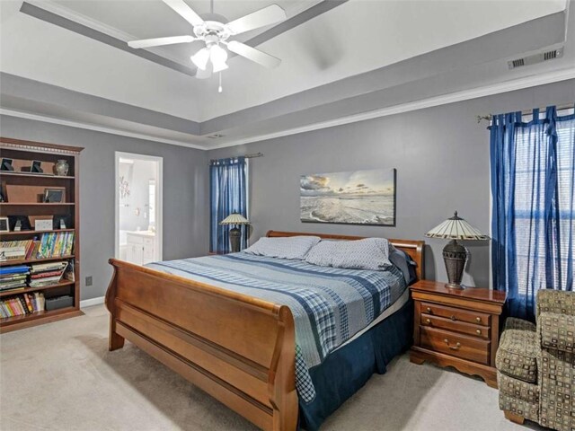 bedroom featuring connected bathroom, crown molding, light carpet, a tray ceiling, and ceiling fan