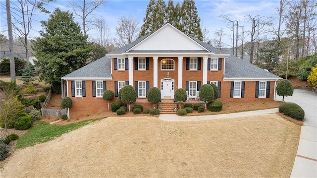 greek revival house with driveway, brick siding, and roof with shingles