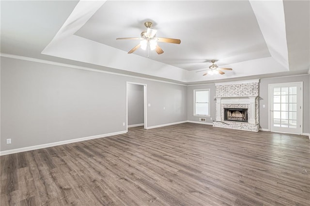 unfurnished living room featuring a fireplace, a tray ceiling, dark wood-type flooring, and plenty of natural light