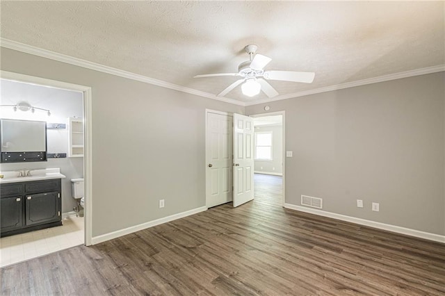 unfurnished bedroom with ceiling fan, a textured ceiling, wood-type flooring, ornamental molding, and ensuite bath