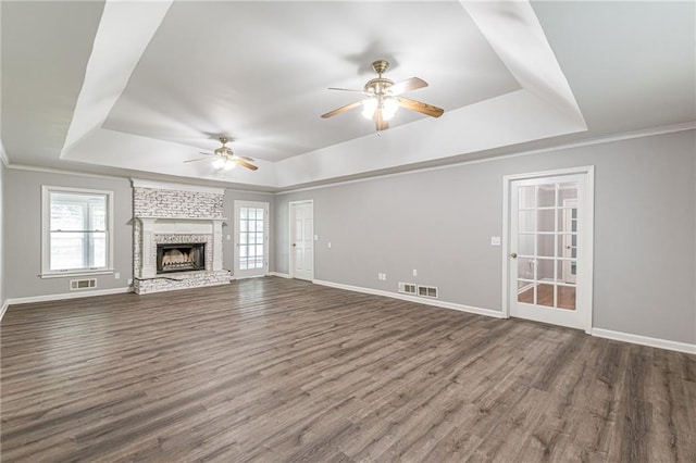 unfurnished living room with a brick fireplace, dark hardwood / wood-style floors, a tray ceiling, and ceiling fan