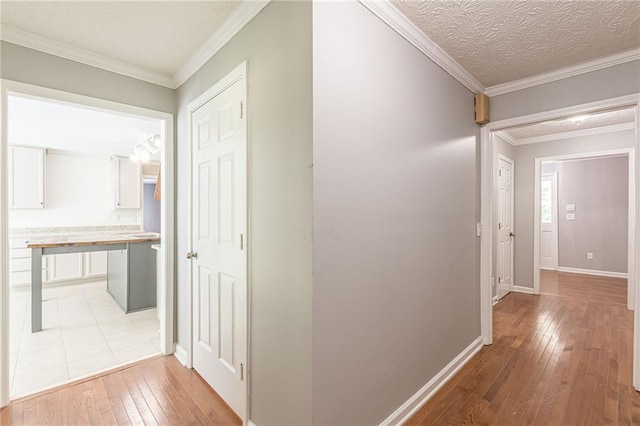 hallway featuring ornamental molding, a textured ceiling, and light wood-type flooring