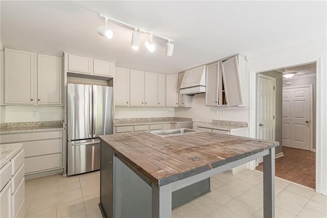 kitchen with light wood-type flooring, a center island, custom range hood, stainless steel refrigerator, and track lighting