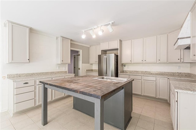 kitchen with stainless steel fridge, butcher block countertops, white cabinetry, and a center island