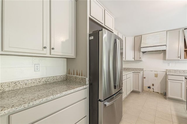 kitchen with white cabinets, stainless steel fridge, light tile patterned floors, premium range hood, and light stone countertops