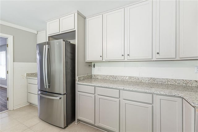 kitchen featuring ornamental molding, stainless steel fridge, light tile patterned floors, white cabinetry, and light stone counters