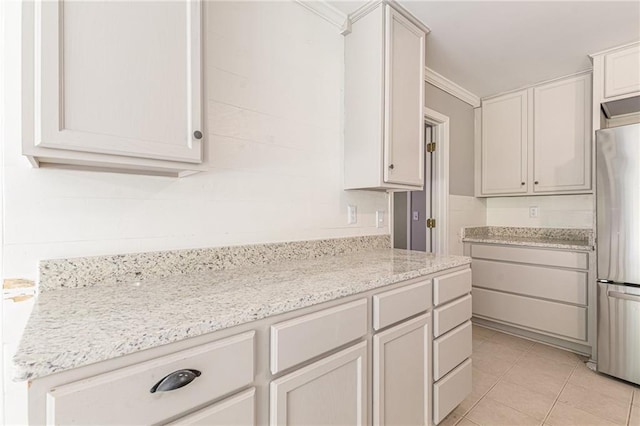 kitchen featuring ornamental molding, light stone countertops, light tile patterned floors, white cabinets, and stainless steel refrigerator