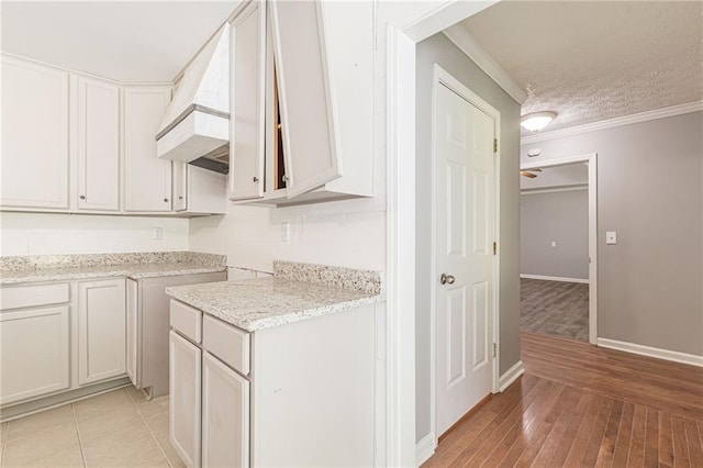 kitchen with custom exhaust hood, white cabinets, a textured ceiling, ornamental molding, and light hardwood / wood-style floors