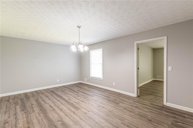 empty room with a notable chandelier, a textured ceiling, and hardwood / wood-style floors