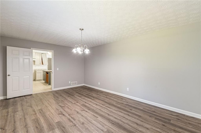 spare room with light hardwood / wood-style flooring, a textured ceiling, and a chandelier