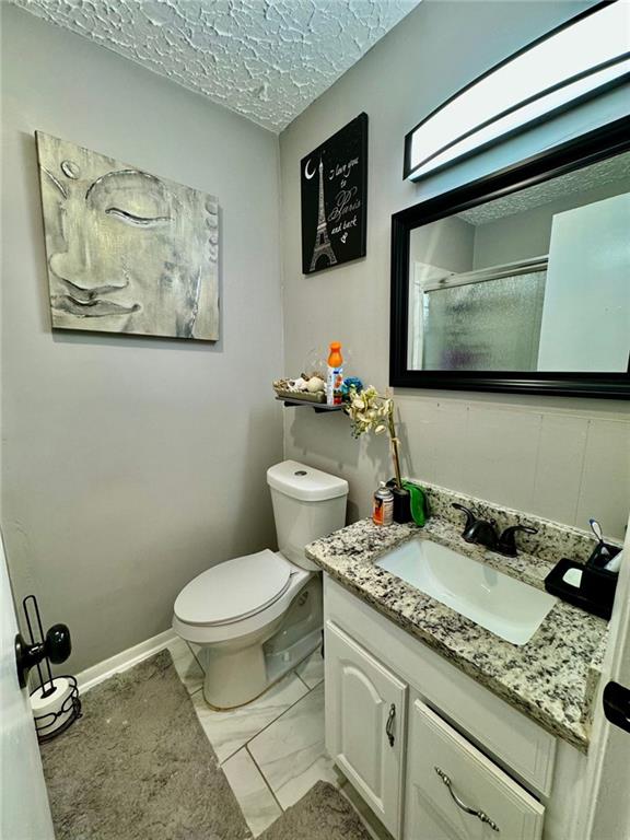 312 E Broad St, Winder, GA 30680 - bathroom featuring toilet, vanity, marble finish floors, a shower, and a textured ceiling