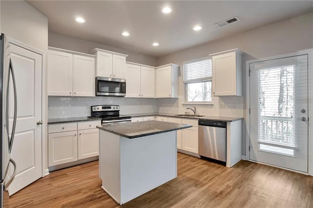 kitchen with appliances with stainless steel finishes, white cabinetry, light hardwood / wood-style floors, a kitchen island, and dark stone counters