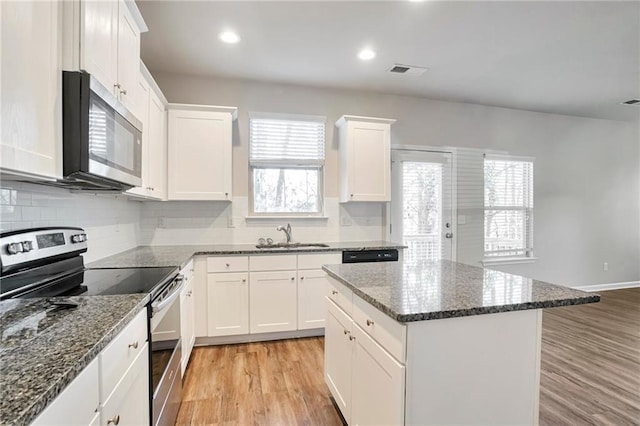 kitchen with sink, light hardwood / wood-style flooring, appliances with stainless steel finishes, white cabinetry, and dark stone countertops