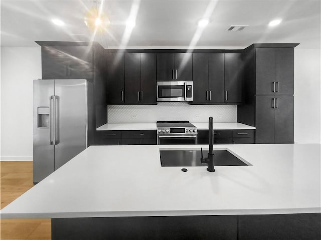 kitchen featuring decorative backsplash, light hardwood / wood-style floors, an island with sink, and stainless steel appliances