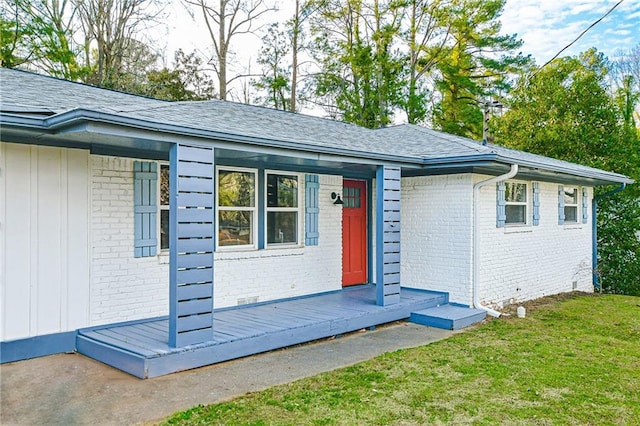 exterior space with brick siding, a yard, and roof with shingles