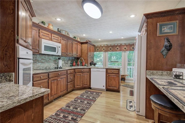 kitchen with sink, white appliances, light hardwood / wood-style flooring, and light stone counters