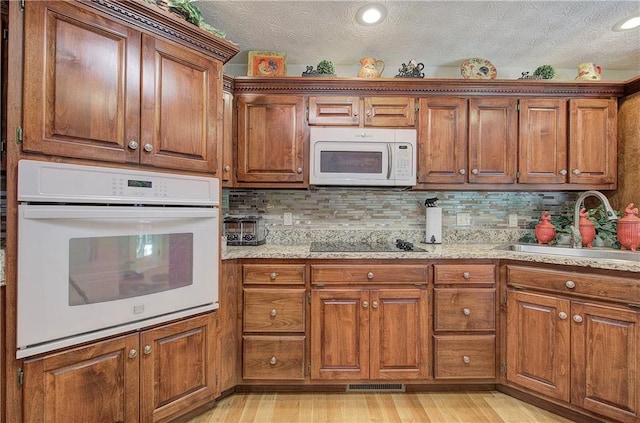 kitchen featuring a textured ceiling, white appliances, sink, and light hardwood / wood-style flooring