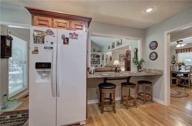 kitchen with a kitchen breakfast bar, white fridge with ice dispenser, light hardwood / wood-style floors, and a textured ceiling