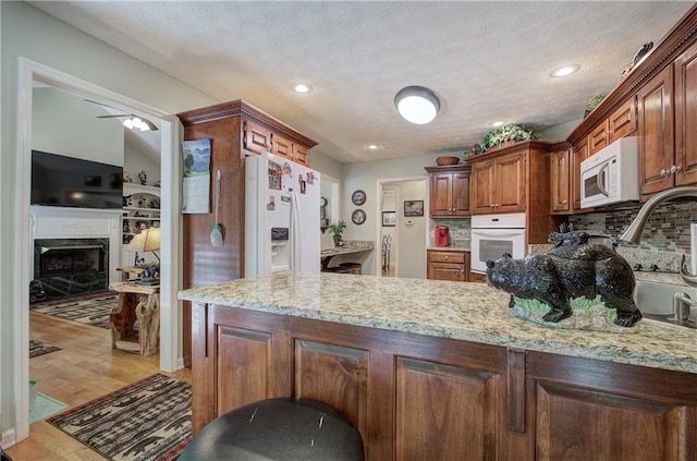 kitchen featuring backsplash, kitchen peninsula, light hardwood / wood-style floors, and white appliances