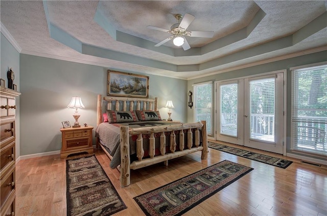 bedroom featuring access to outside, light hardwood / wood-style floors, a raised ceiling, and ceiling fan