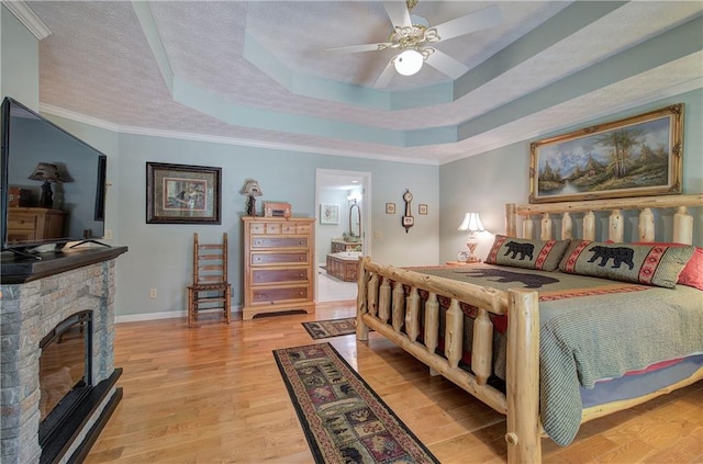 bedroom with ceiling fan, ornamental molding, connected bathroom, a tray ceiling, and light hardwood / wood-style floors