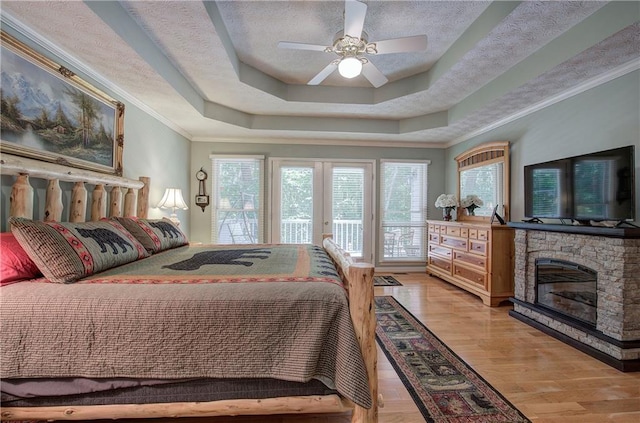 bedroom with ceiling fan, light hardwood / wood-style flooring, ornamental molding, a tray ceiling, and access to outside