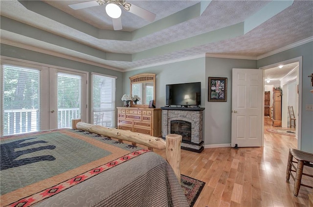 bedroom with ornamental molding, a raised ceiling, ceiling fan, hardwood / wood-style flooring, and a stone fireplace