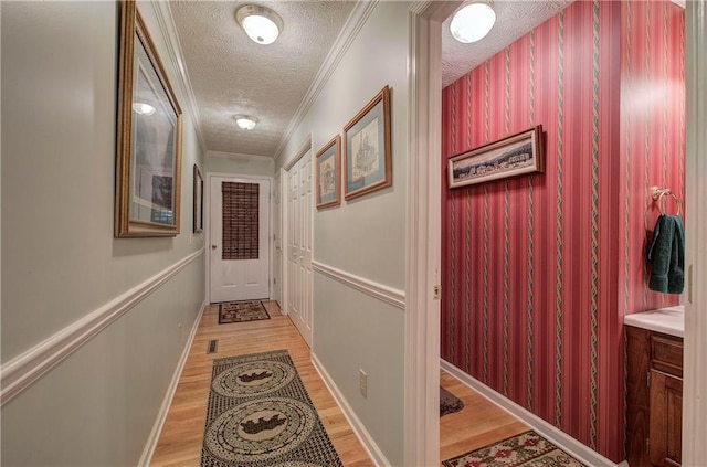 hall with light hardwood / wood-style floors, ornamental molding, and a textured ceiling