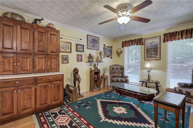 living area featuring ceiling fan, light hardwood / wood-style flooring, a textured ceiling, and ornamental molding