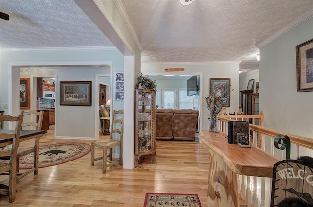 corridor with ornamental molding, a textured ceiling, and light hardwood / wood-style flooring