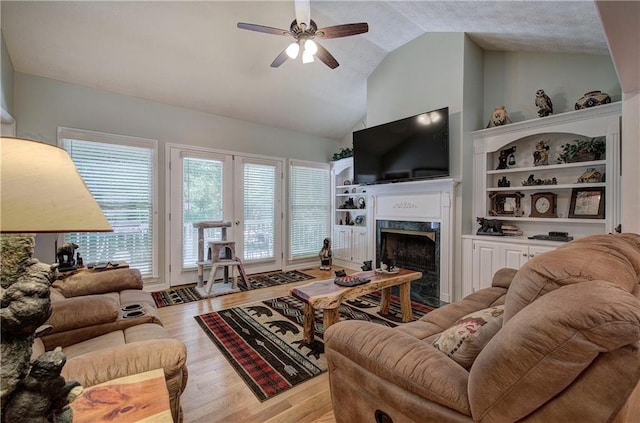 living room with a premium fireplace, ceiling fan, lofted ceiling, and light wood-type flooring