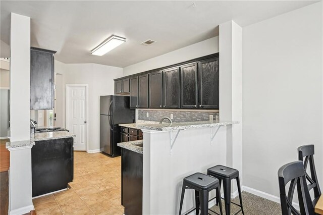 2726 Pierce Brennen Ct, Lawrenceville, GA 30043 - kitchen featuring a breakfast bar area, visible vents, a peninsula, freestanding refrigerator, and decorative backsplash