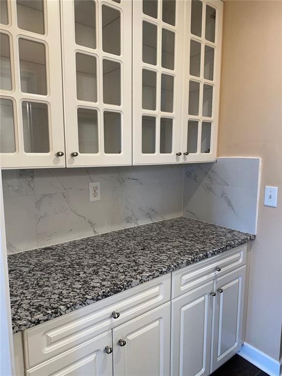 3381 Walkers Ridge Rd, Dacula, GA 30019 - kitchen featuring decorative backsplash, dark stone countertops, white cabinets, glass insert cabinets, and baseboards