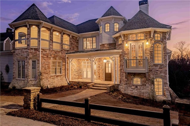 view of front of home with a fenced front yard, a balcony, stone siding, and a chimney