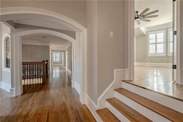 hallway featuring ornamental molding, wood finished floors, baseboards, arched walkways, and an upstairs landing