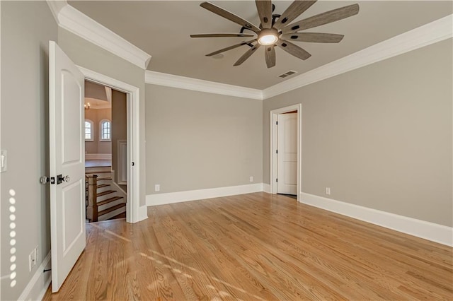 empty room featuring a ceiling fan, baseboards, light wood-type flooring, visible vents, and ornamental molding
