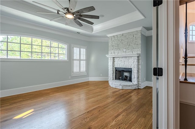 unfurnished living room with ornamental molding, a raised ceiling, a ceiling fan, and wood finished floors