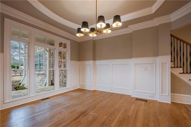 unfurnished room with stairs, wood finished floors, a decorative wall, a wainscoted wall, and a notable chandelier