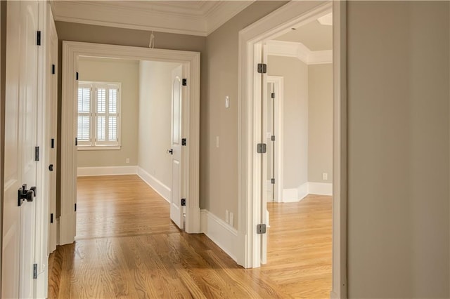 hallway featuring crown molding, baseboards, and light wood-type flooring