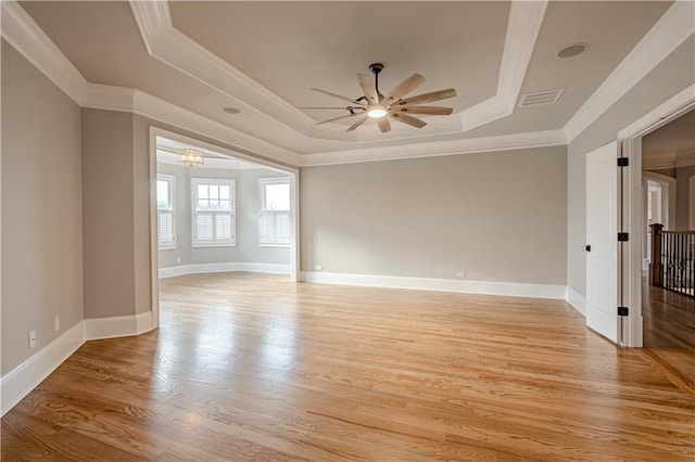 empty room featuring crown molding, ceiling fan with notable chandelier, light wood-type flooring, a tray ceiling, and visible vents