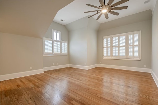 interior space featuring ceiling fan, visible vents, light wood-style flooring, baseboards, and vaulted ceiling