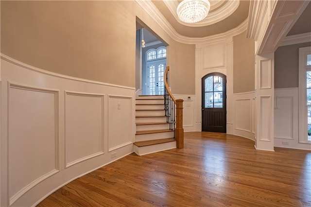 foyer featuring an inviting chandelier, a decorative wall, wood finished floors, a wealth of natural light, and ornamental molding