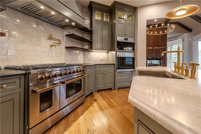 kitchen with light wood-type flooring, gray cabinets, range with two ovens, custom range hood, and a notable chandelier