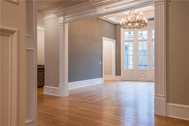 spare room featuring crown molding, light wood finished floors, ornate columns, and a chandelier