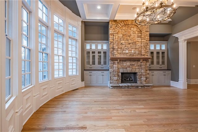 unfurnished living room featuring a stone fireplace, visible vents, an inviting chandelier, coffered ceiling, and light wood-style flooring