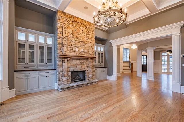 unfurnished living room featuring decorative columns, a fireplace, a chandelier, coffered ceiling, and light wood-style flooring